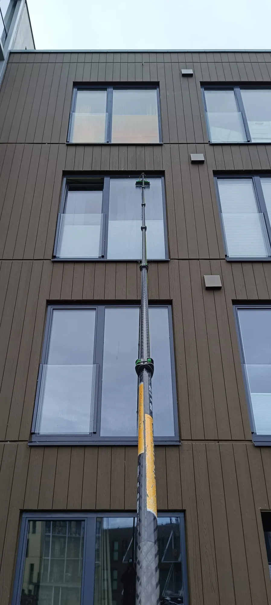 Akende välipesu teleskoopharja ja veega hoone fassaadil