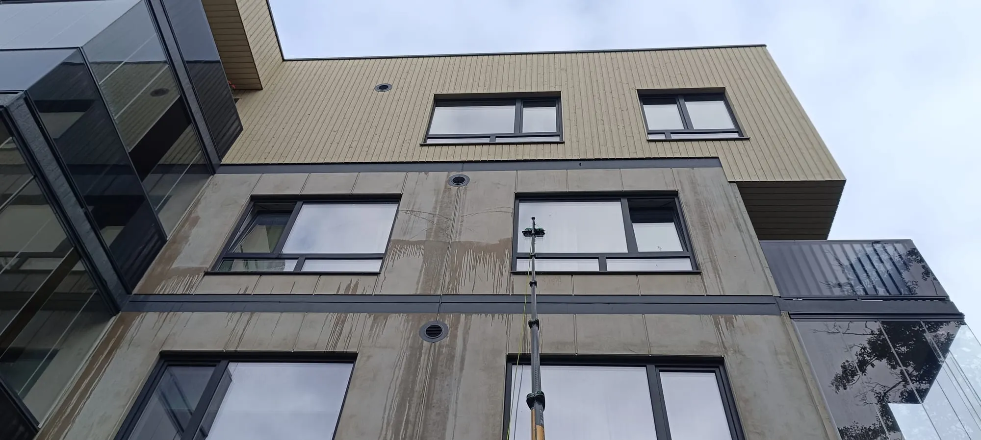 Teleskoop-puhastusvarras pesemas korterelamu fassaadiaknaid väljastpoolt
