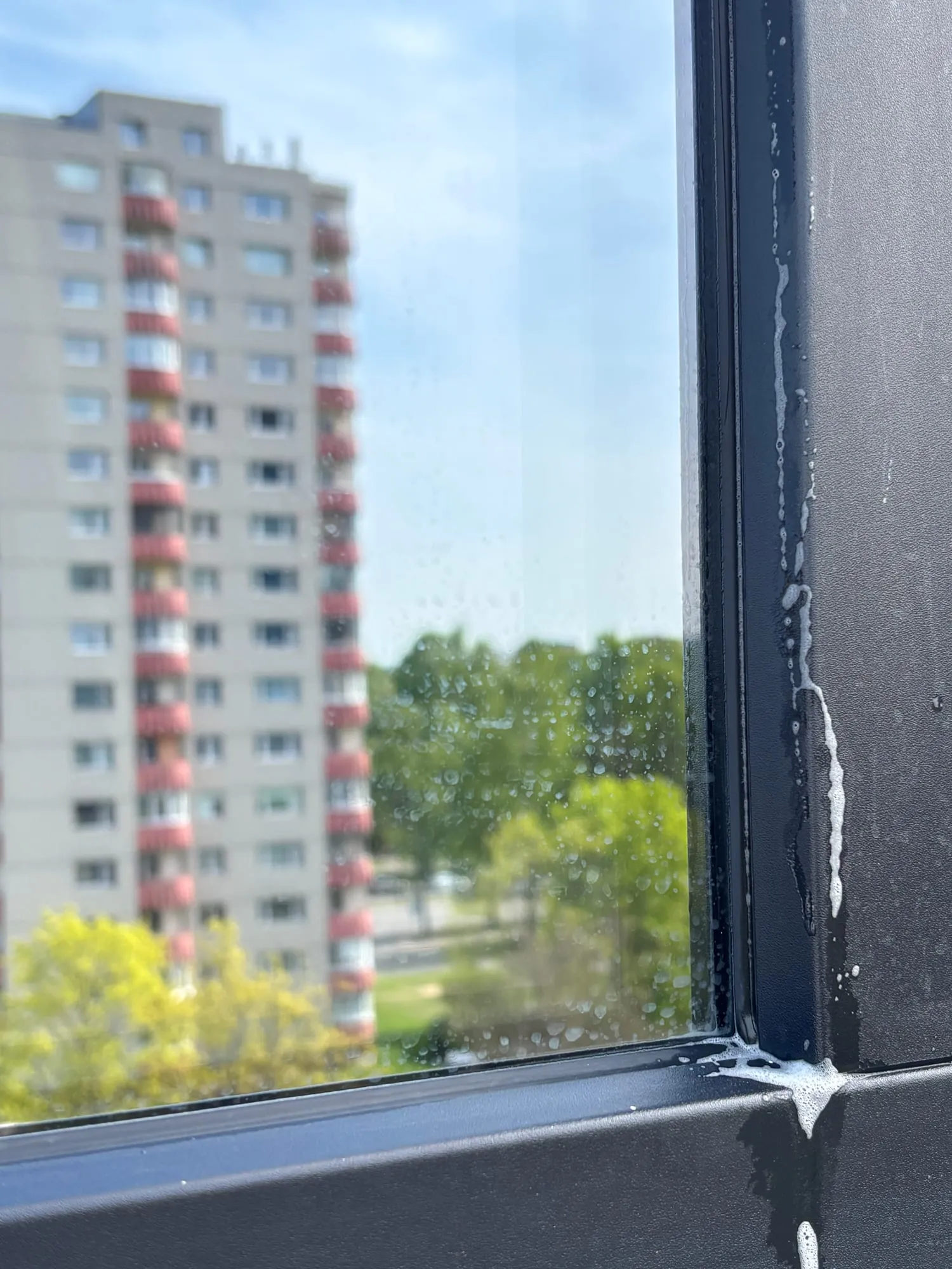 Pesuvahuga aken kõrghoones akende välispesu käigus, taustal naaberhoone