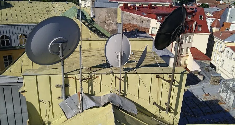 Vanad satelliitantennid mastide ja tõmmitsatega plekk-katusel, taustal Tallinna vanalinna katused