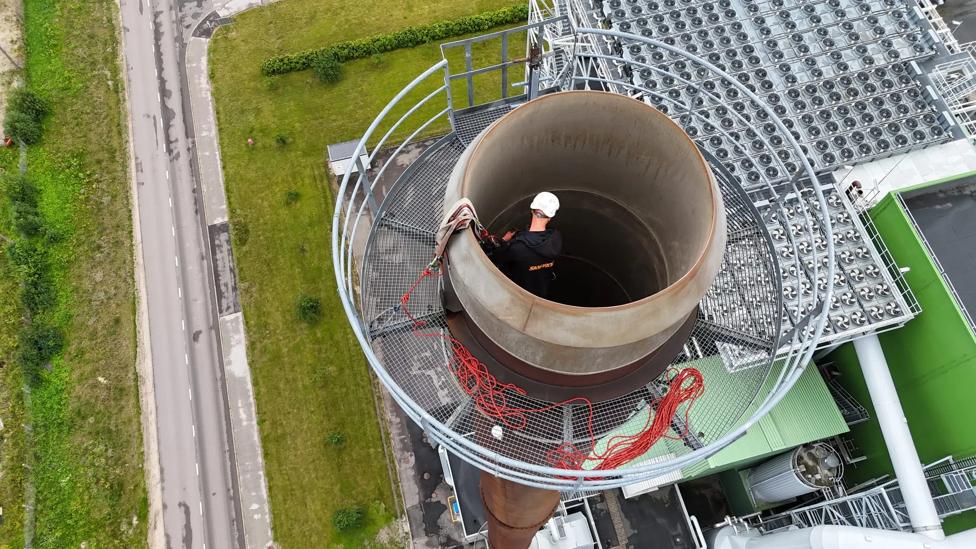 Kõrgtööde tehnik korstna tipu platvormil suitsulõõri avause juures, kõrval punased köied — elektrijaama korstna inspektsioon Pärnus