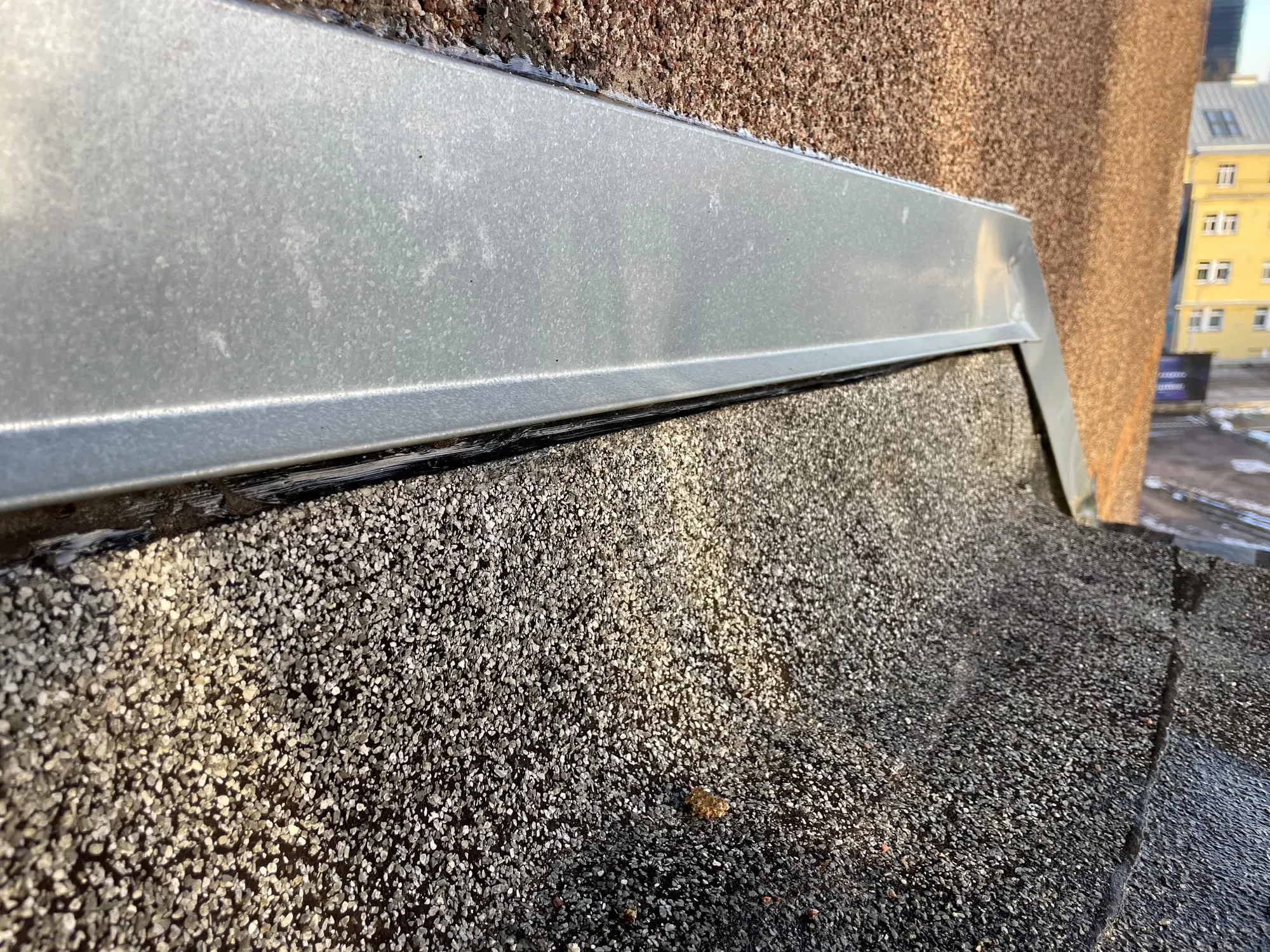 Korterelamu fassaadi kivikarniisile paigaldatud uus plekk-kate ja värske tihendus, taustal linnavaade
