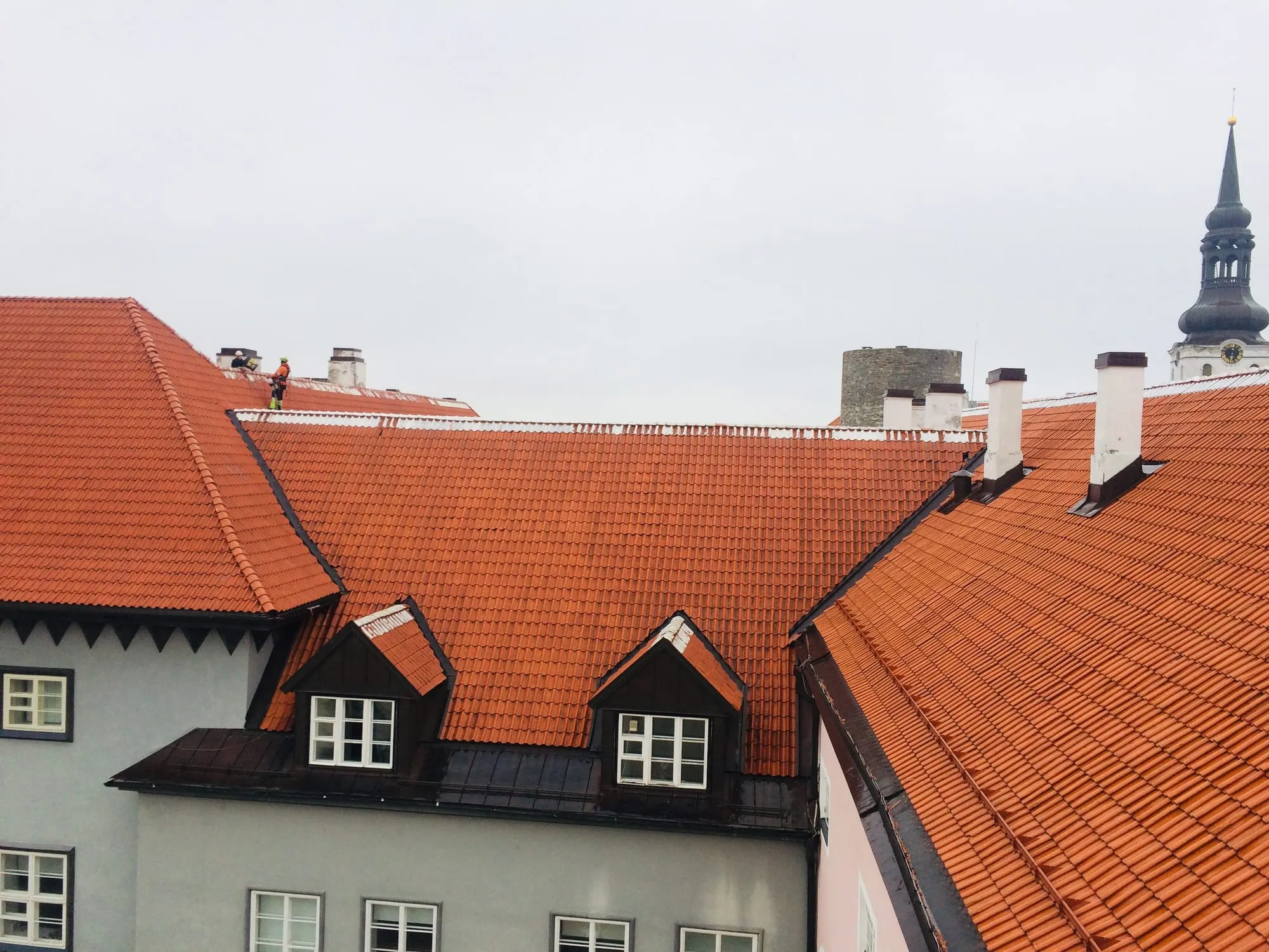 Tehnik oranžis tööriietuses ajaloolise hoone punase kivikatuse harjal Toompeal, taustal Toomkiriku tornikiiver