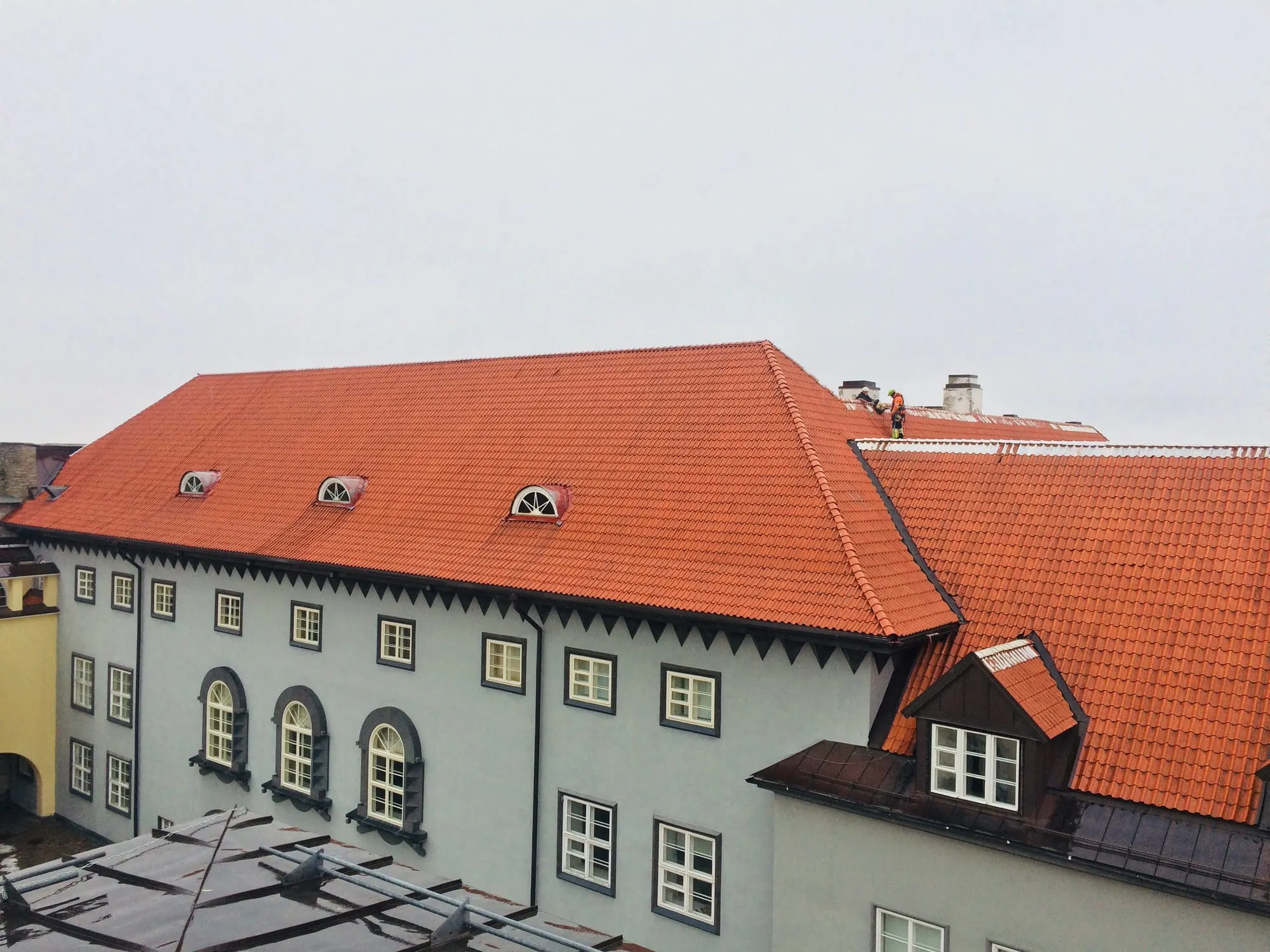 Kaks tehnikut ajaloolise hoone punase kivikatuse harjal katusetöid tegemas