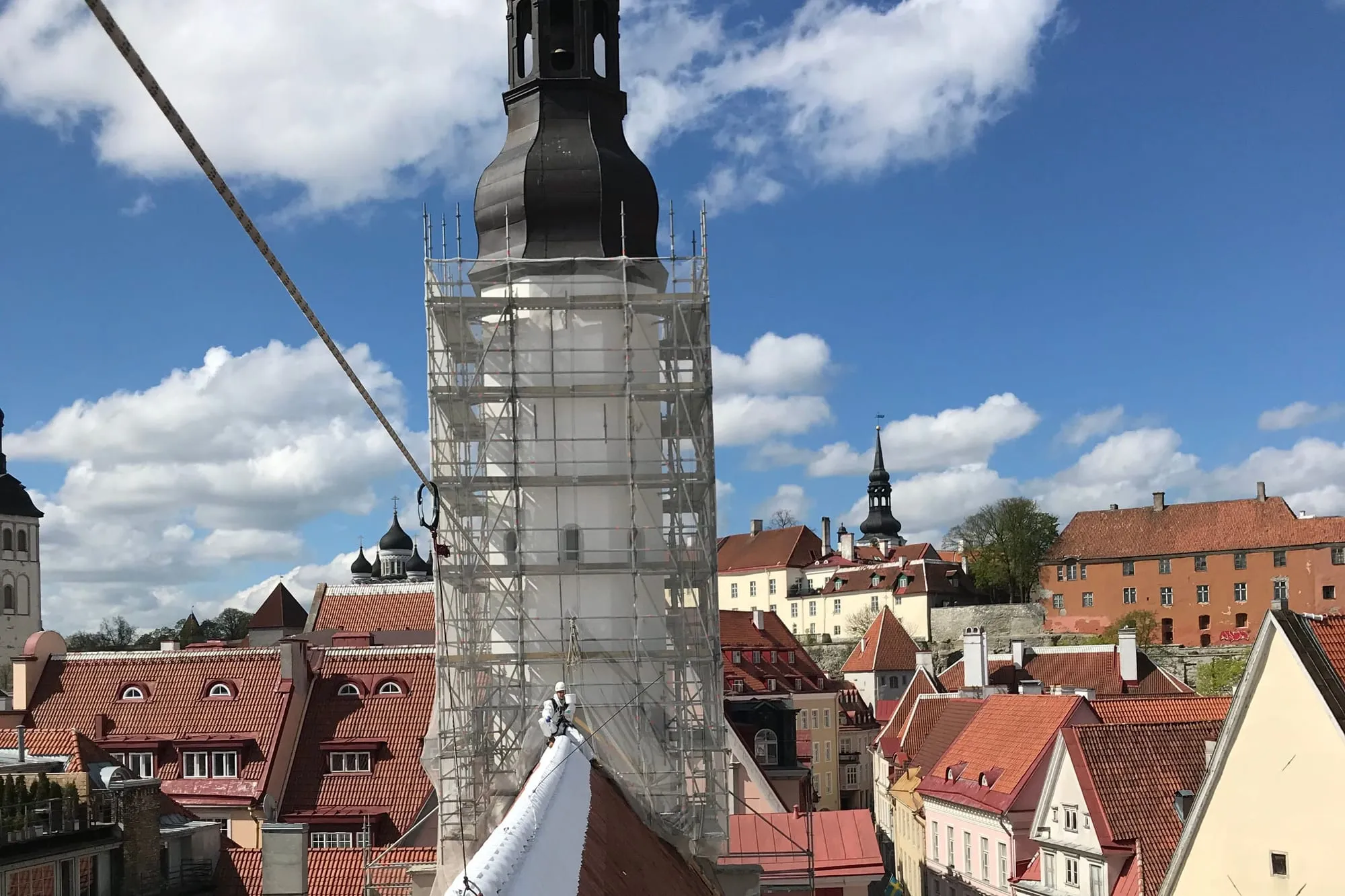 Köiega julgestatud tehnik seisab Pühavaimu kiriku värskelt valgeks värvitud katuseharjal, taustal tellingutes kirikutorn ja Tallinna vanalinn.