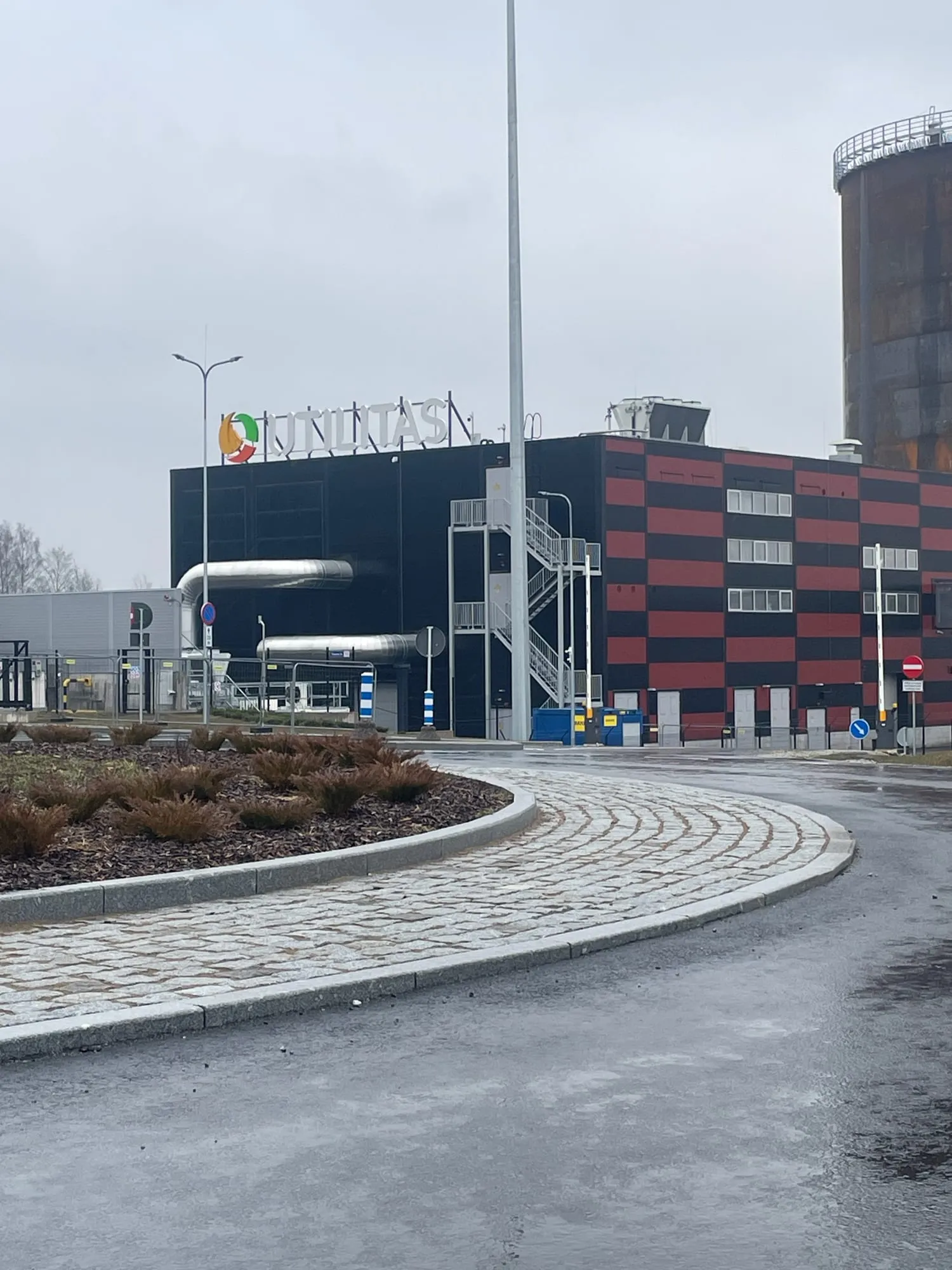 Elektrijaama hoone välisvaade, katuseservas valgustatud ettevõtte logo ja taamal kõrge metallist rajatis