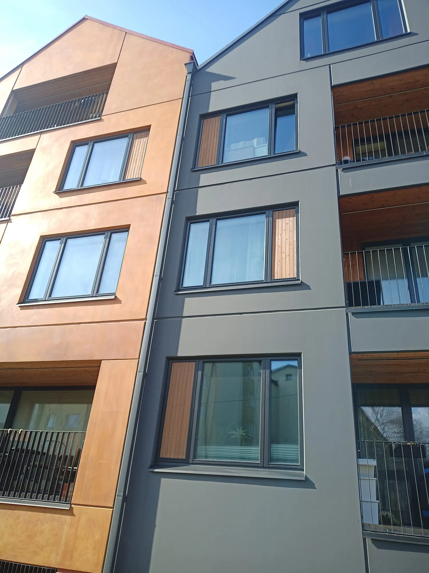 Korterelamu fassaad selges päikesevalguses, värskelt õlitatud puitpaneelid akende kõrval