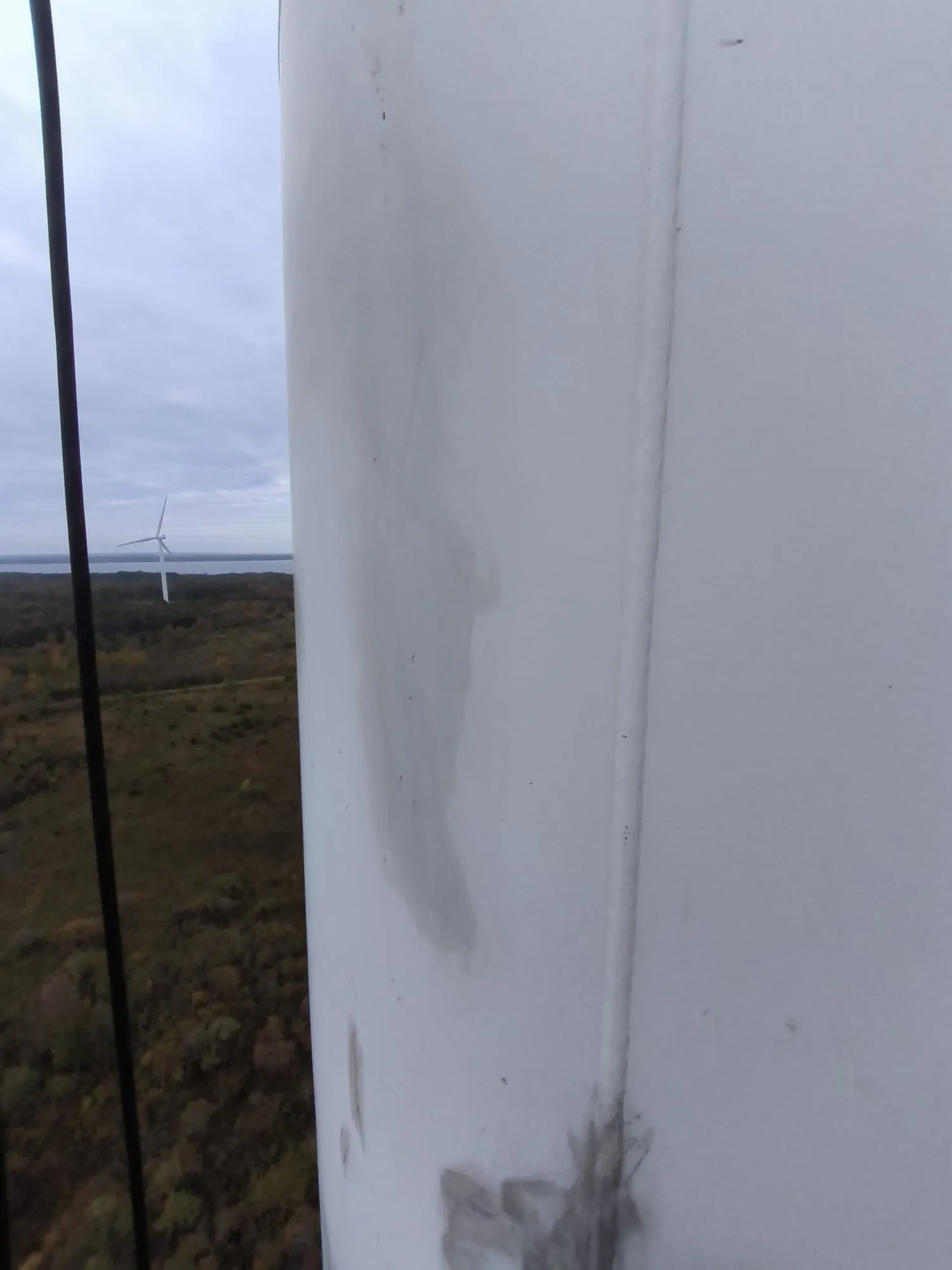 Tuulikutorni valge pind määrdejälgedega, taustal teine tuulik ja mets